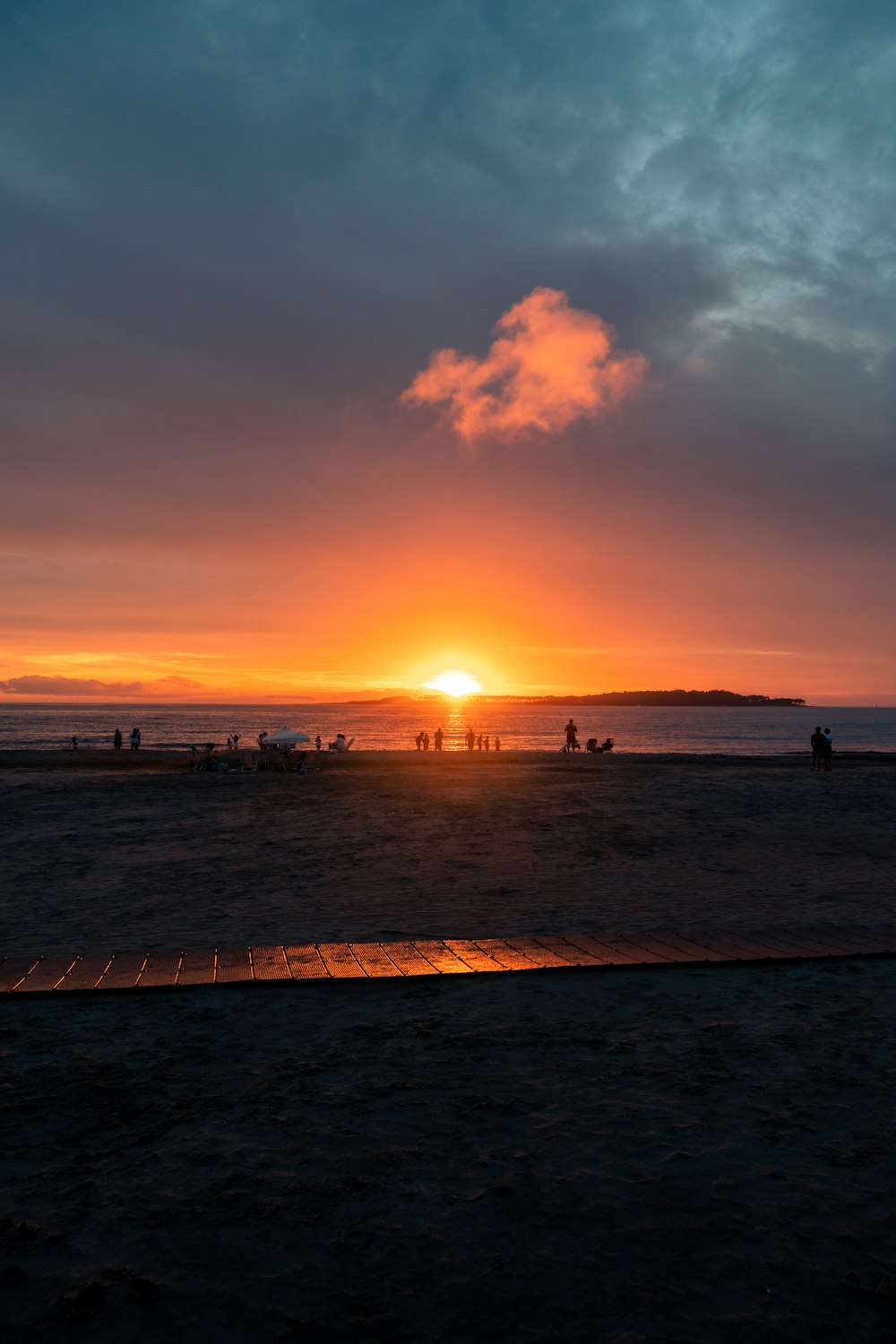 the sun is setting over the ocean with people walking on the beach