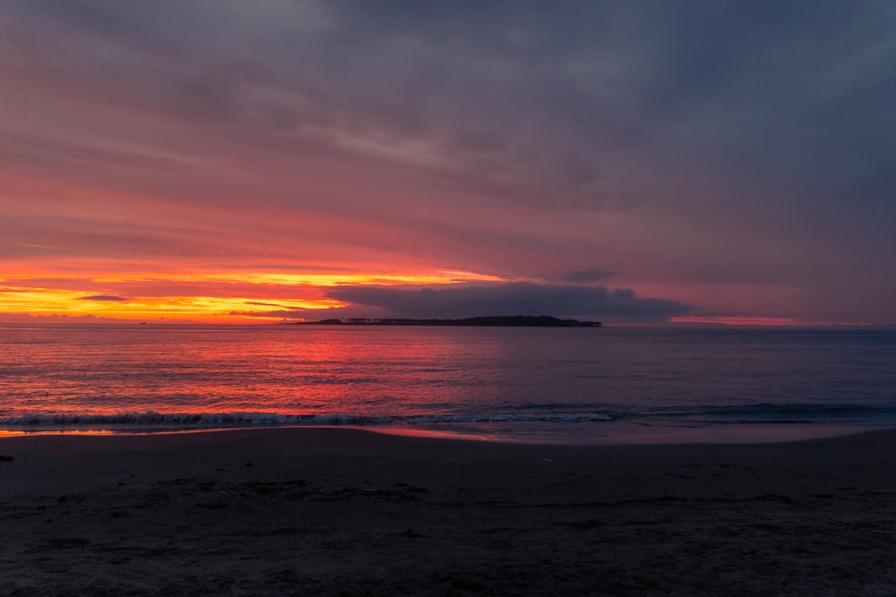 the sun is setting over the ocean on the beach