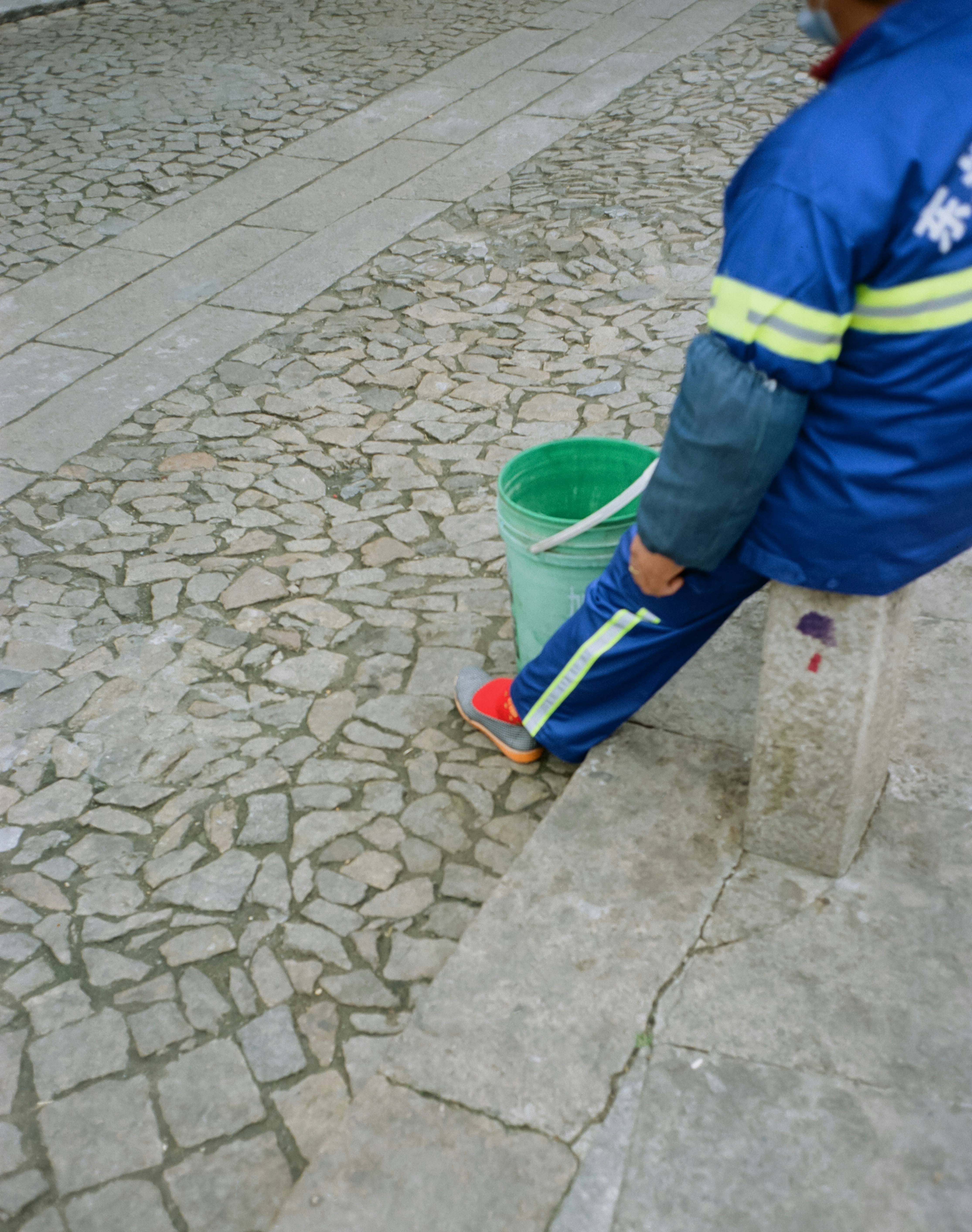 a man sitting on a bench next to a green bucket