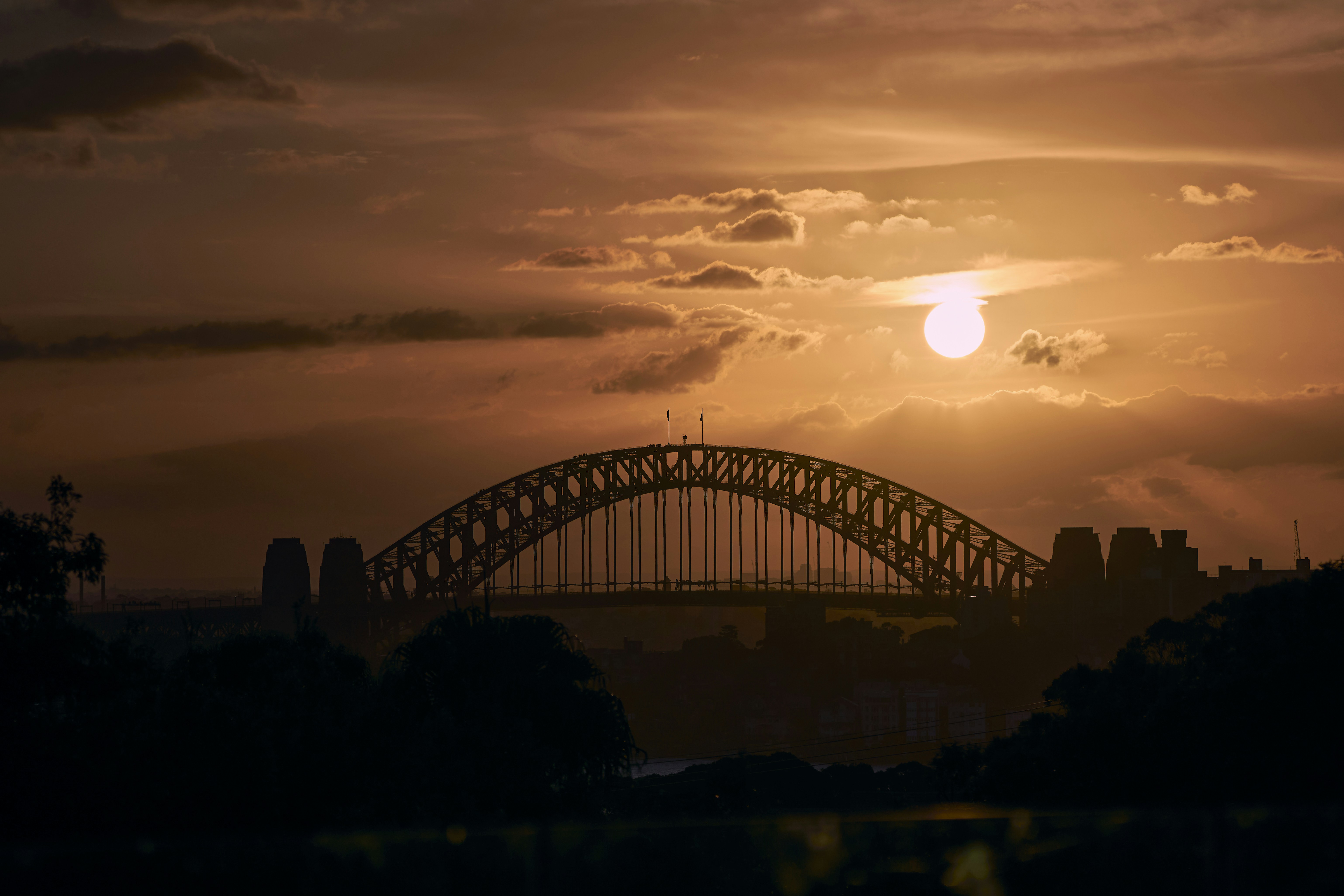 the sun is setting over a bridge in a city