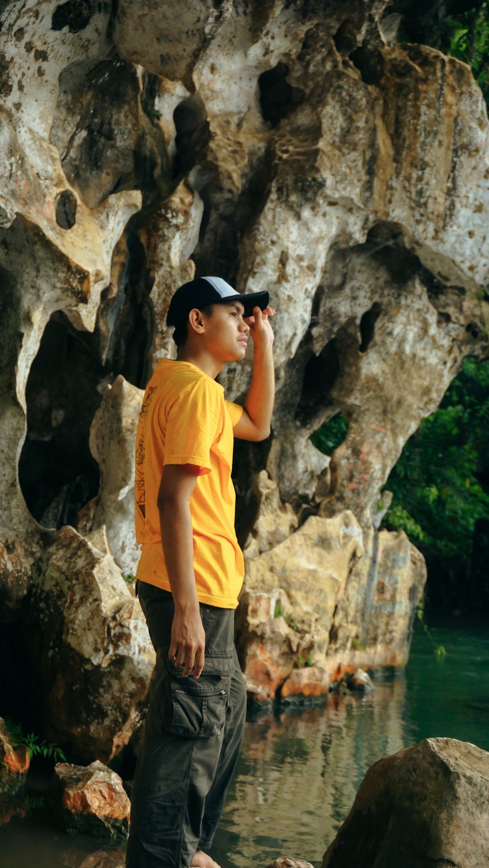 a man in a yellow shirt is standing by some rocks