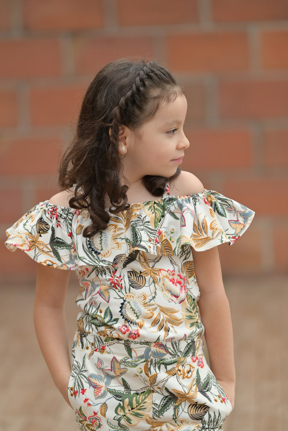 a little girl standing in front of a brick wall