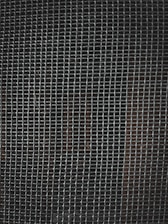 A tightly woven metal grid pattern with small rectangular openings. The background is dark, slightly visible through the mesh.