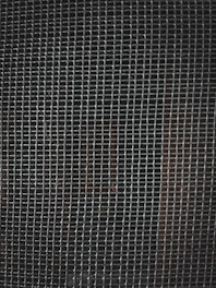 A tightly woven metal grid pattern with small rectangular openings. The background is dark, slightly visible through the mesh.