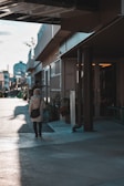 A stylish woman walking through a sunlit city street, carrying a miharo bag over her shoulder.