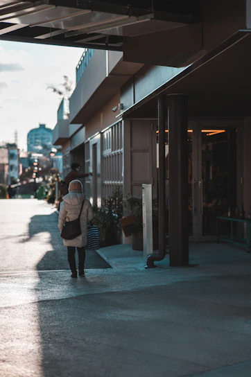 A stylish woman carrying a fosteré bag while walking through a sunlit city street.