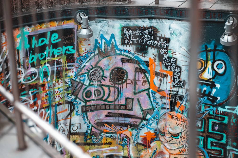 a wall covered in lots of graffiti next to a metal fence