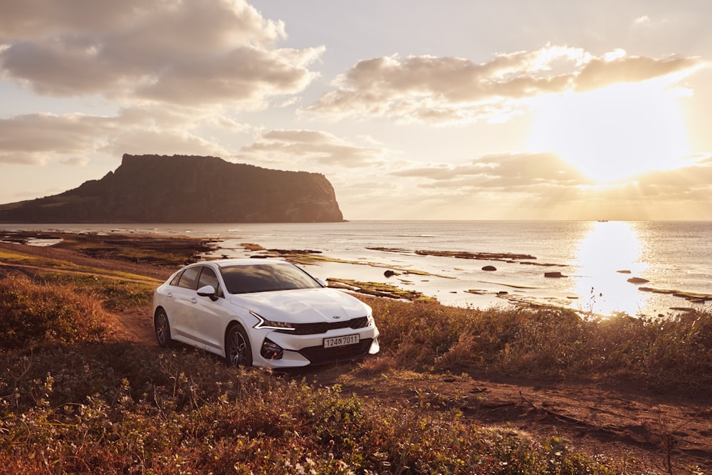 a white car parked on the side of a road next to the ocean