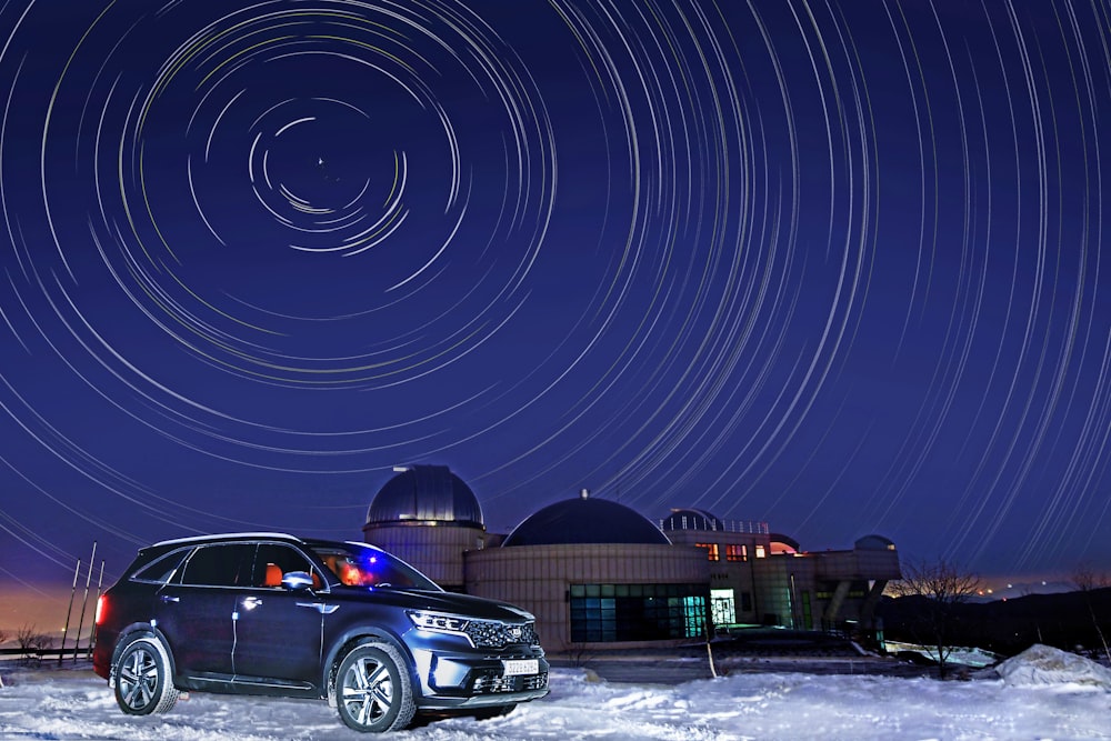 a car parked in front of a building with a star trail in the sky