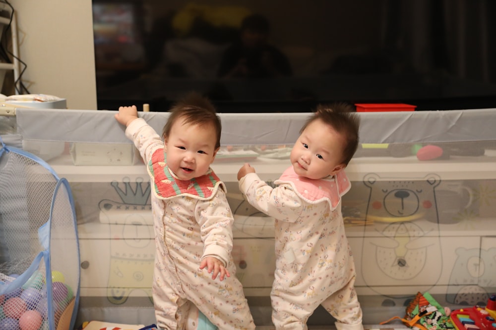 two babies standing next to each other in front of a tv