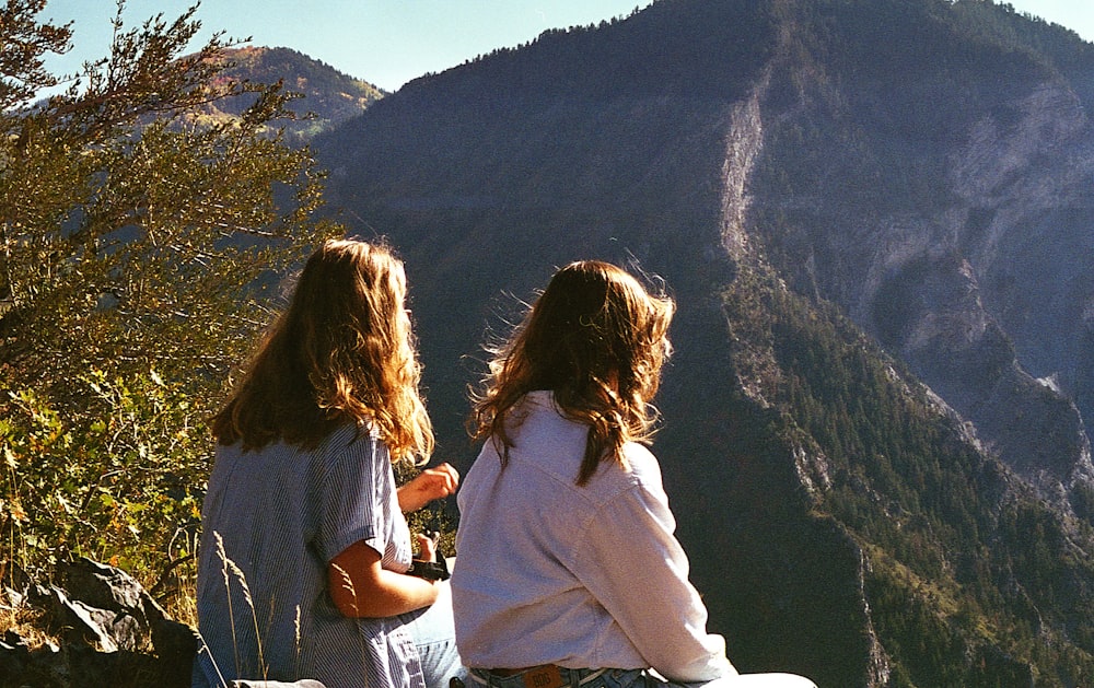 two girls sitting on a rock looking at a mountain