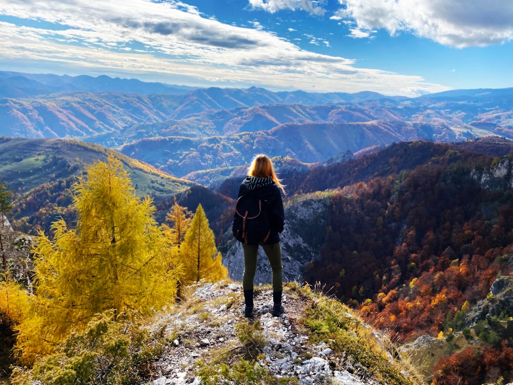 a woman standing on top of a mountain overlooking a valley