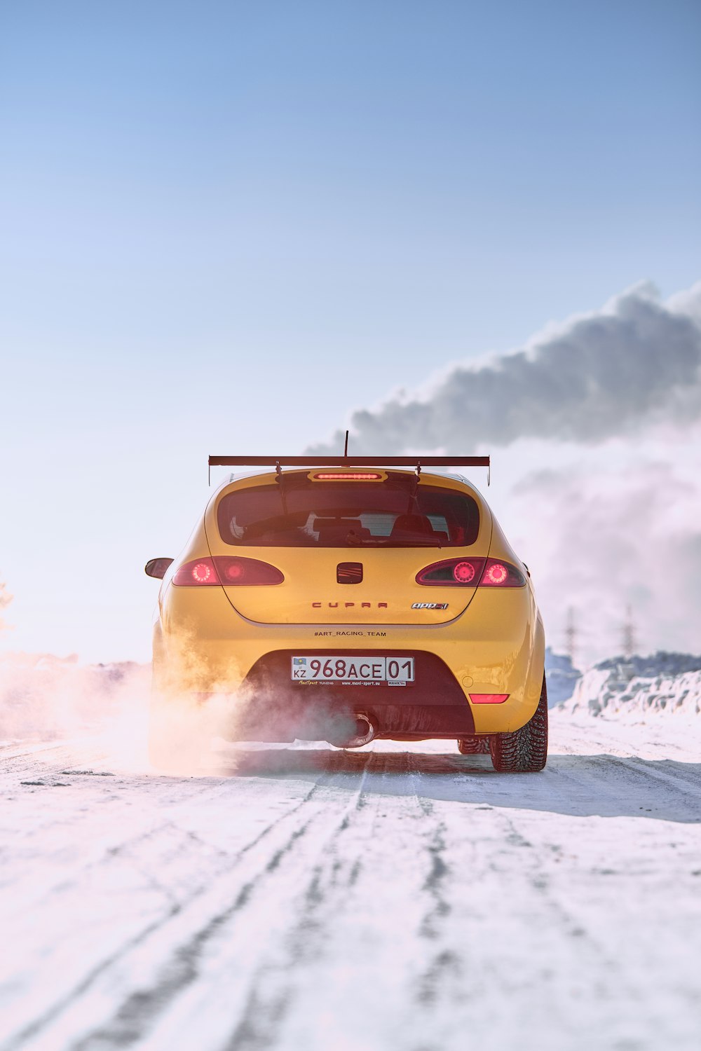 a yellow car driving down a snow covered road