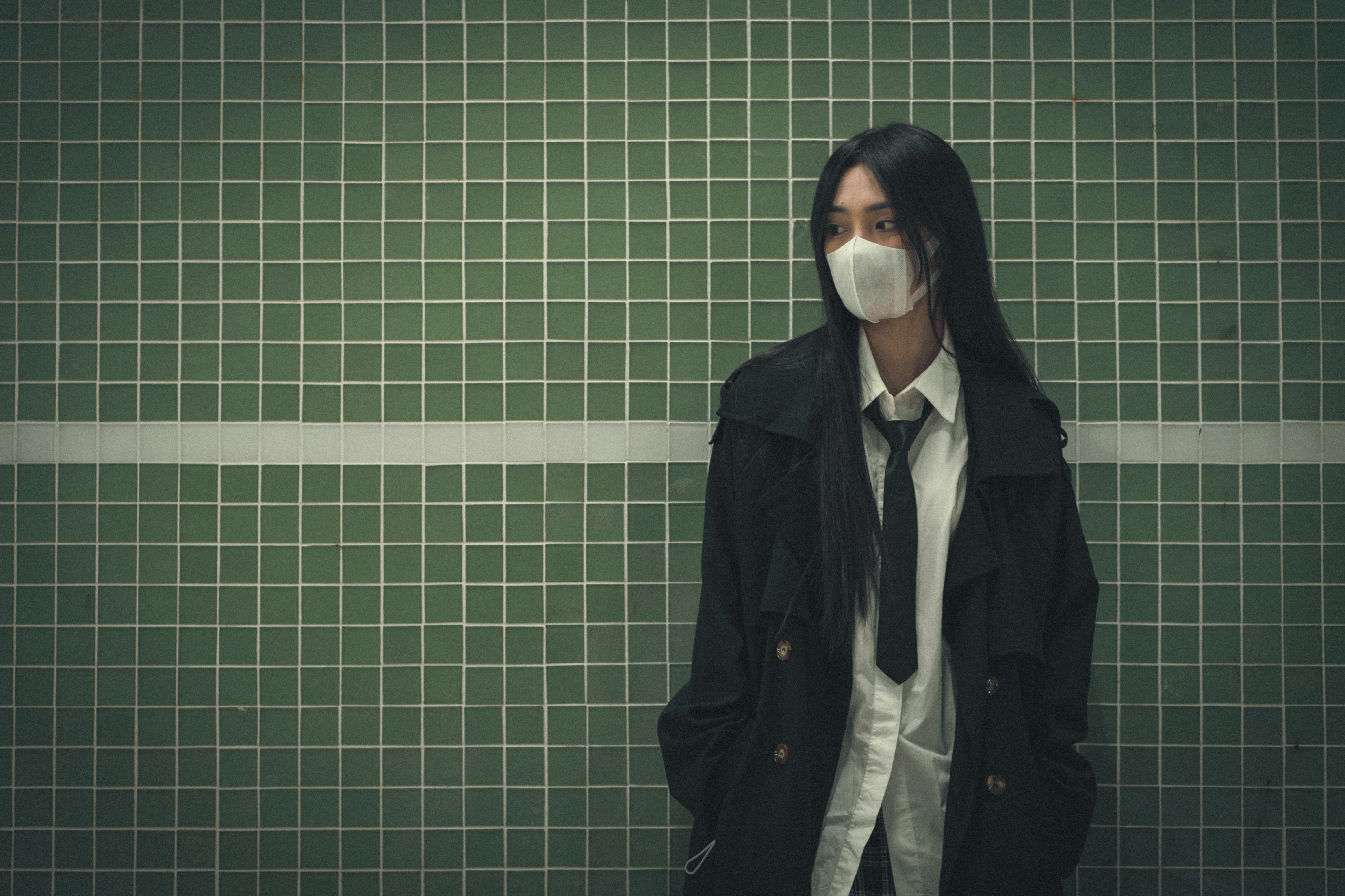 a woman wearing a face mask standing in front of a green tiled wall