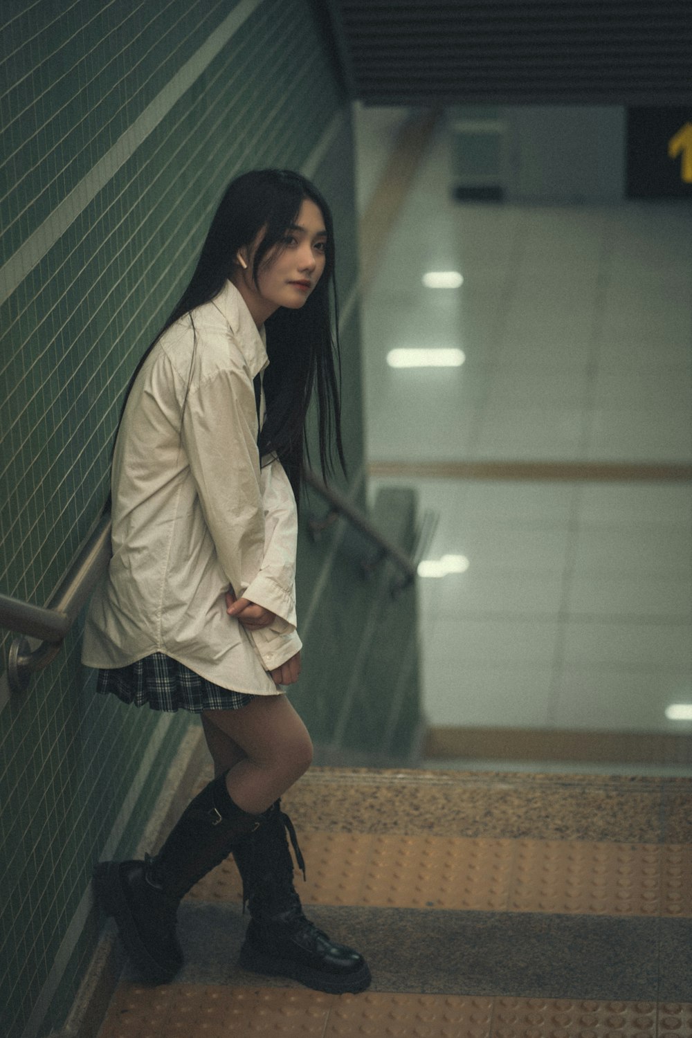 a woman in a white shirt and plaid skirt leaning against a wall