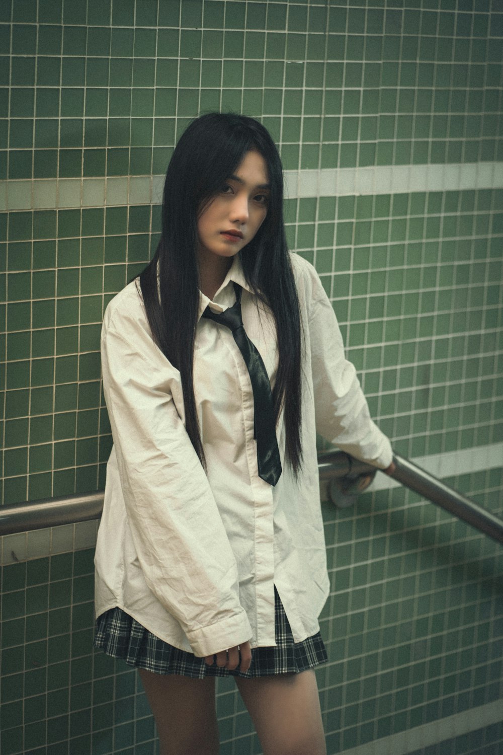 a girl in a school uniform standing in front of a green tiled wall