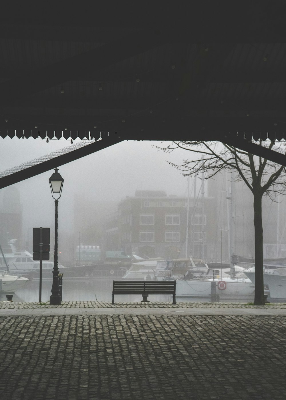 a park bench sitting under a bridge next to a body of water