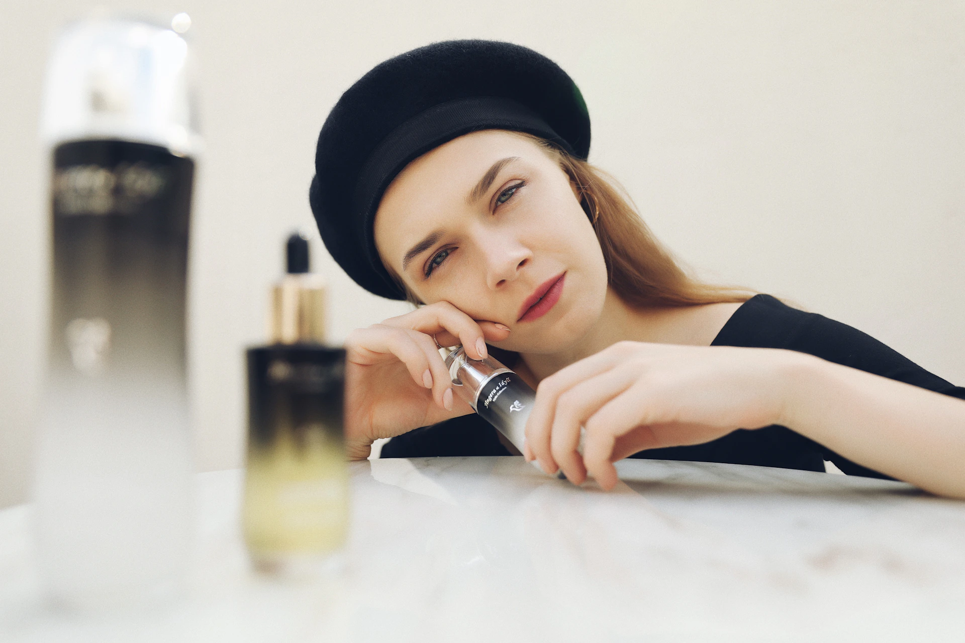 a woman sitting at a table next to a bottle of perfume