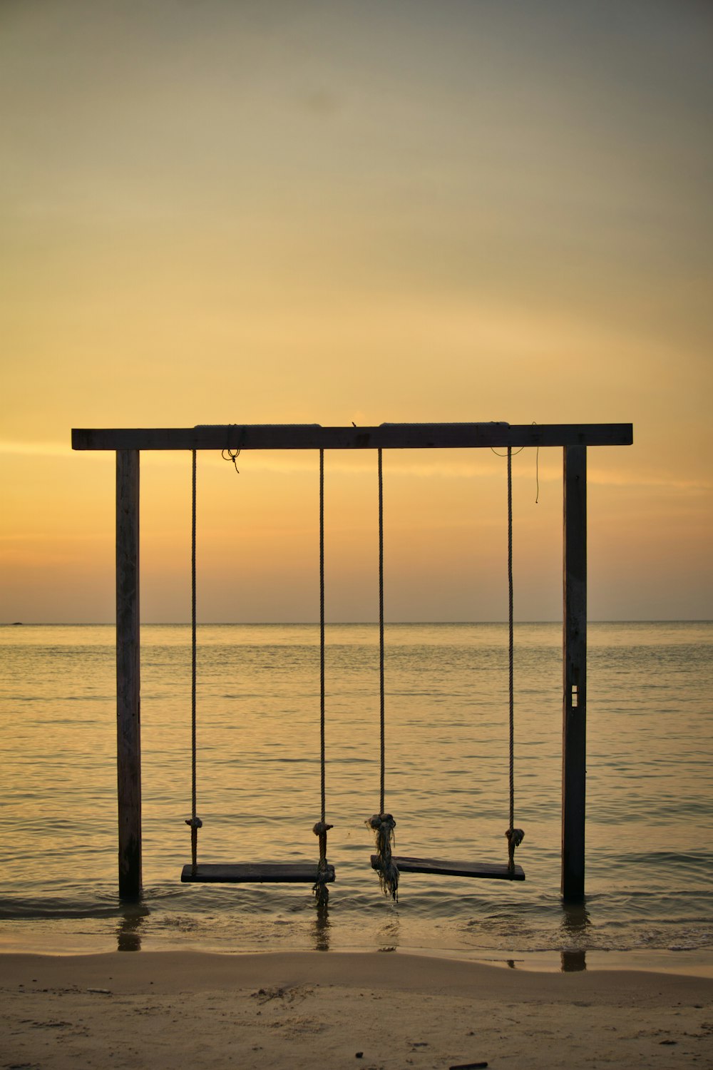 a couple of swings sitting on top of a sandy beach