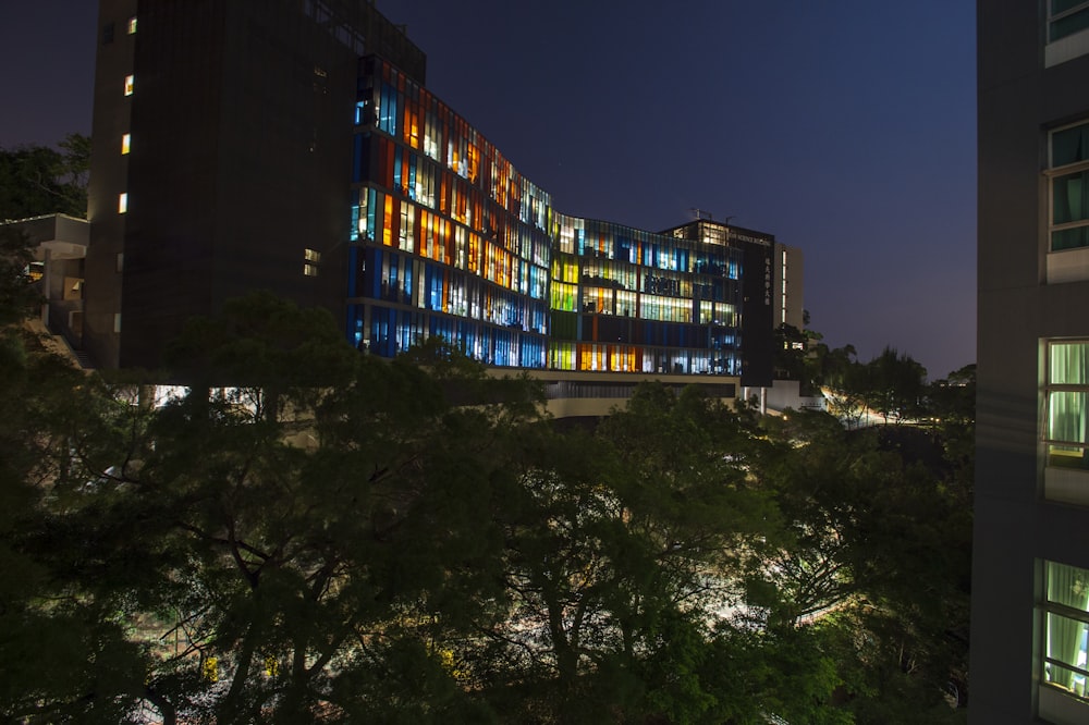 a building lit up at night with trees in front of it