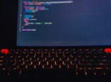 Close-up of hands typing code with neon green backlit keyboard in a dimly lit workspace.