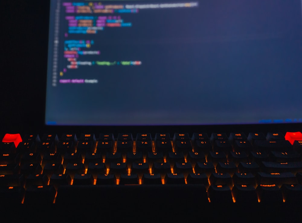 a close up of a keyboard with a computer screen in the background