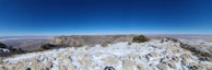 A panoramic view from a rocky summit overlooking rolling mountain ranges.