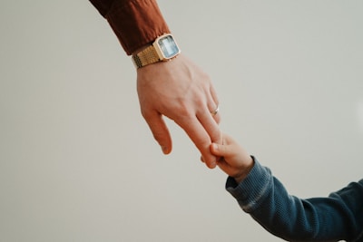 A close-up photo of a child's hand gently holding a caregiver's finger, symbolizing care and connection.