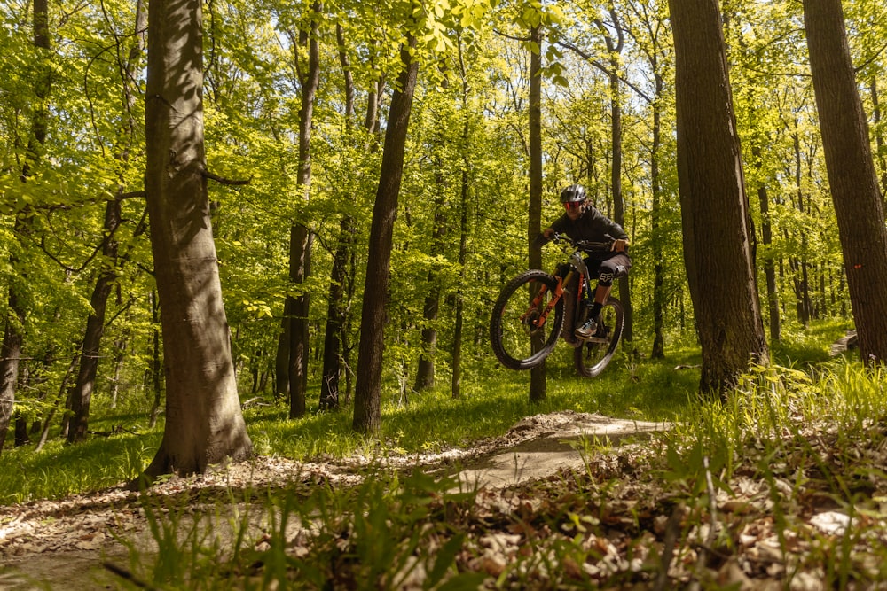 a man riding a bike through a forest filled with trees