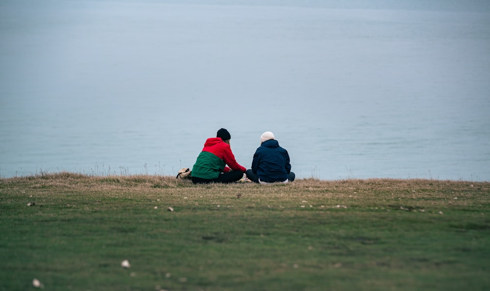 a couple of people sitting on top of a grass covered field