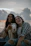 two women sitting on the beach pointing at the camera