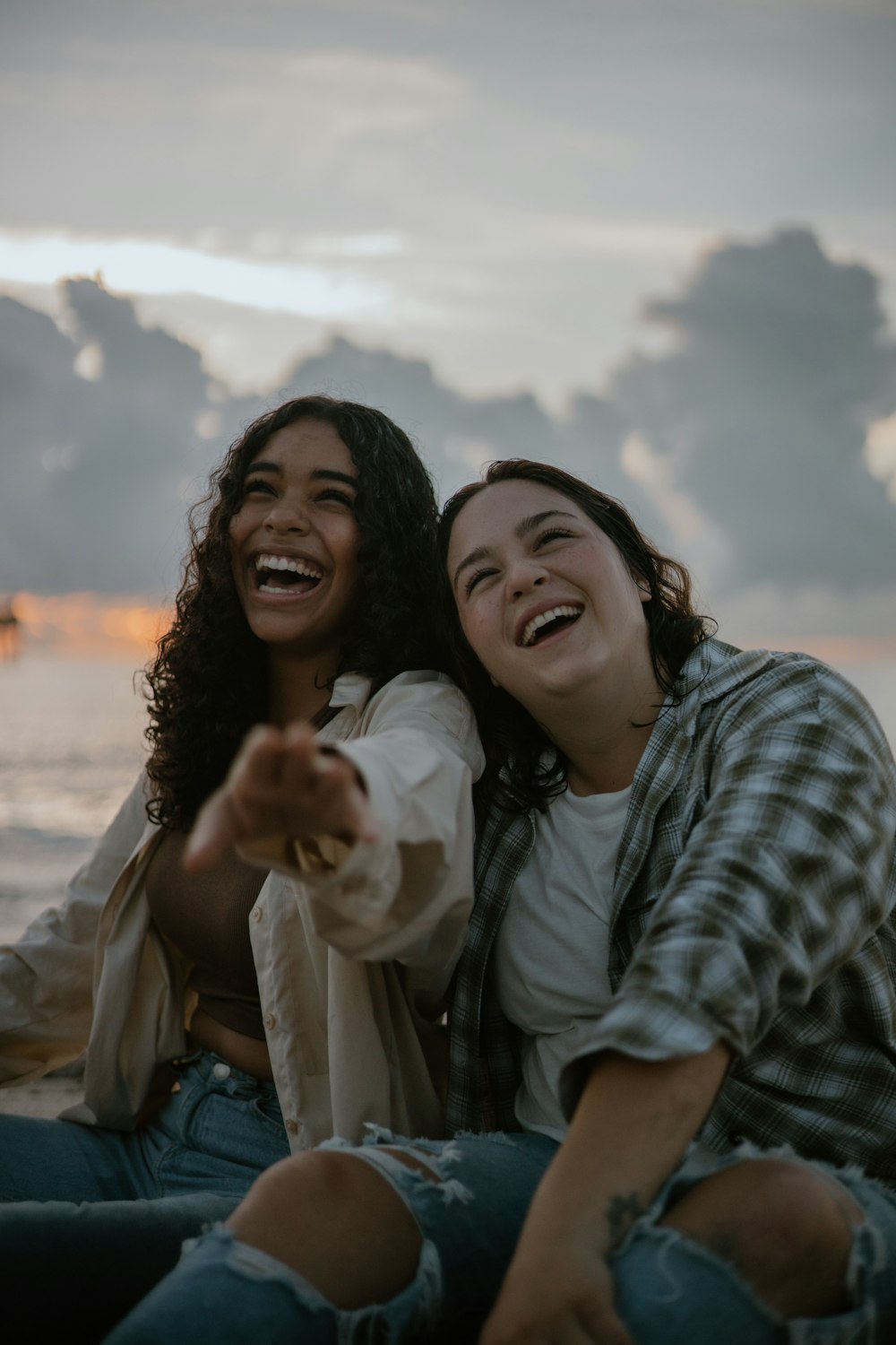 two women sitting on the beach pointing at the camera