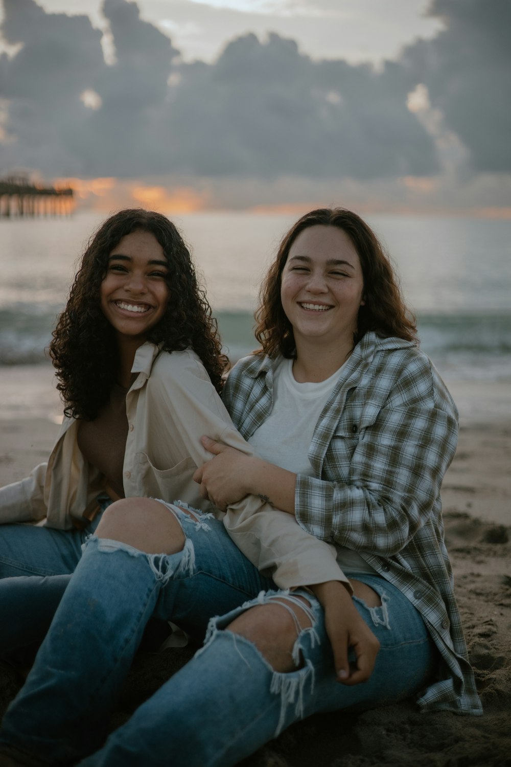 two women sitting on the beach smiling for the camera