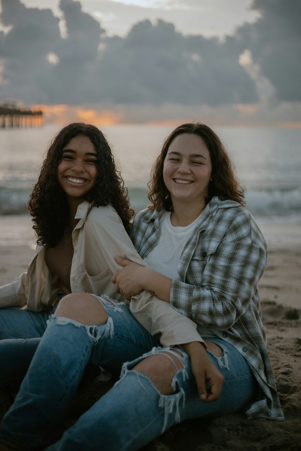 Due donne sedute sulla spiaggia che sorridono per la telecamera