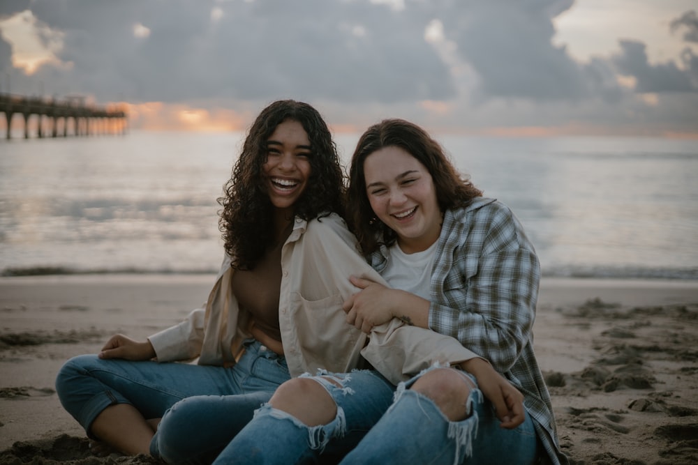 two women sitting on the beach smiling for the camera