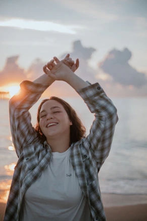 a woman standing on a beach with her hands in the air
