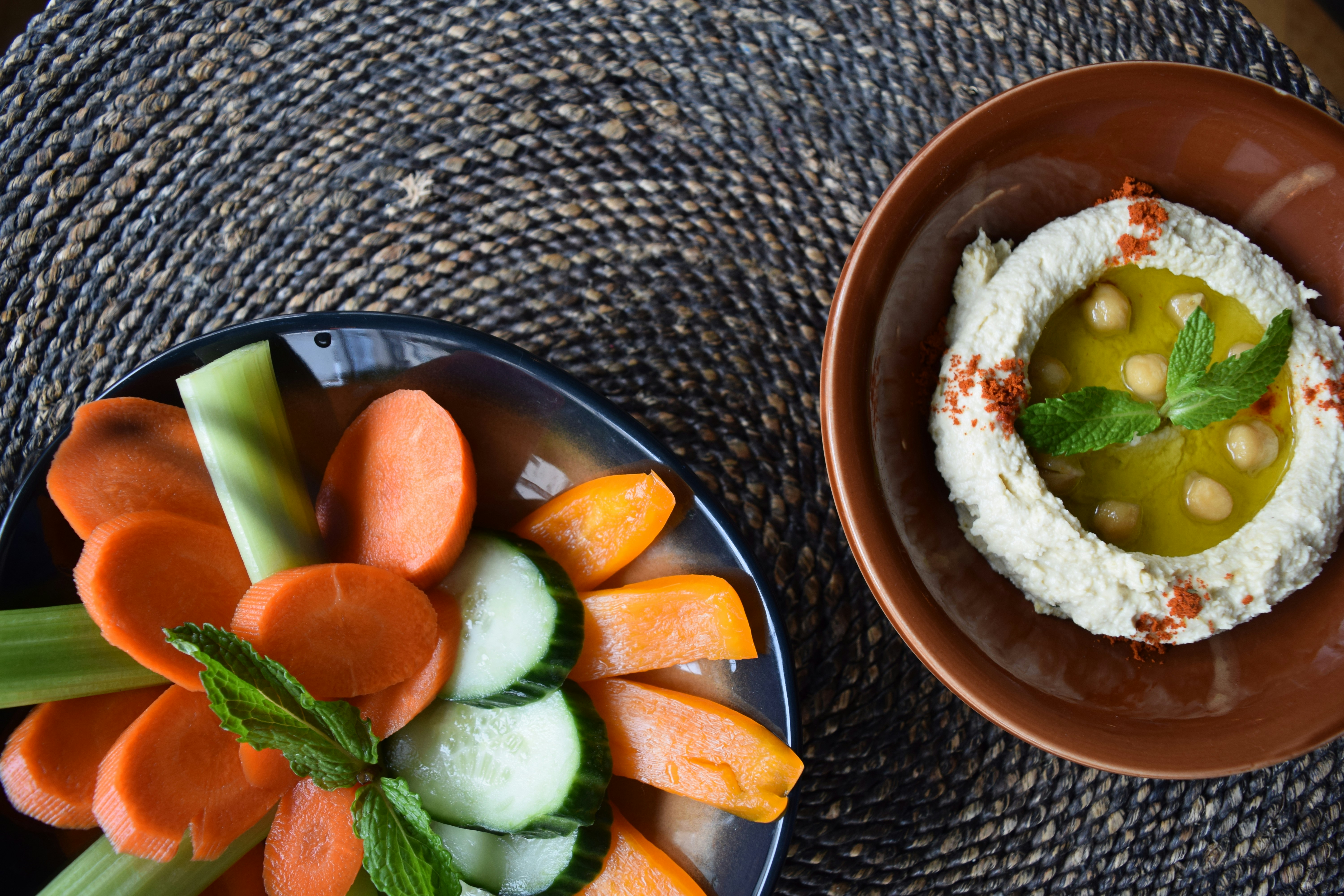 A plate of carrots and celery next to a bowl of hummus