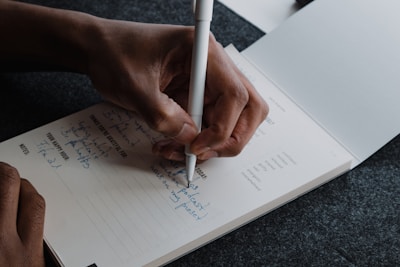 A person writing tasks in a notebook with a pen.