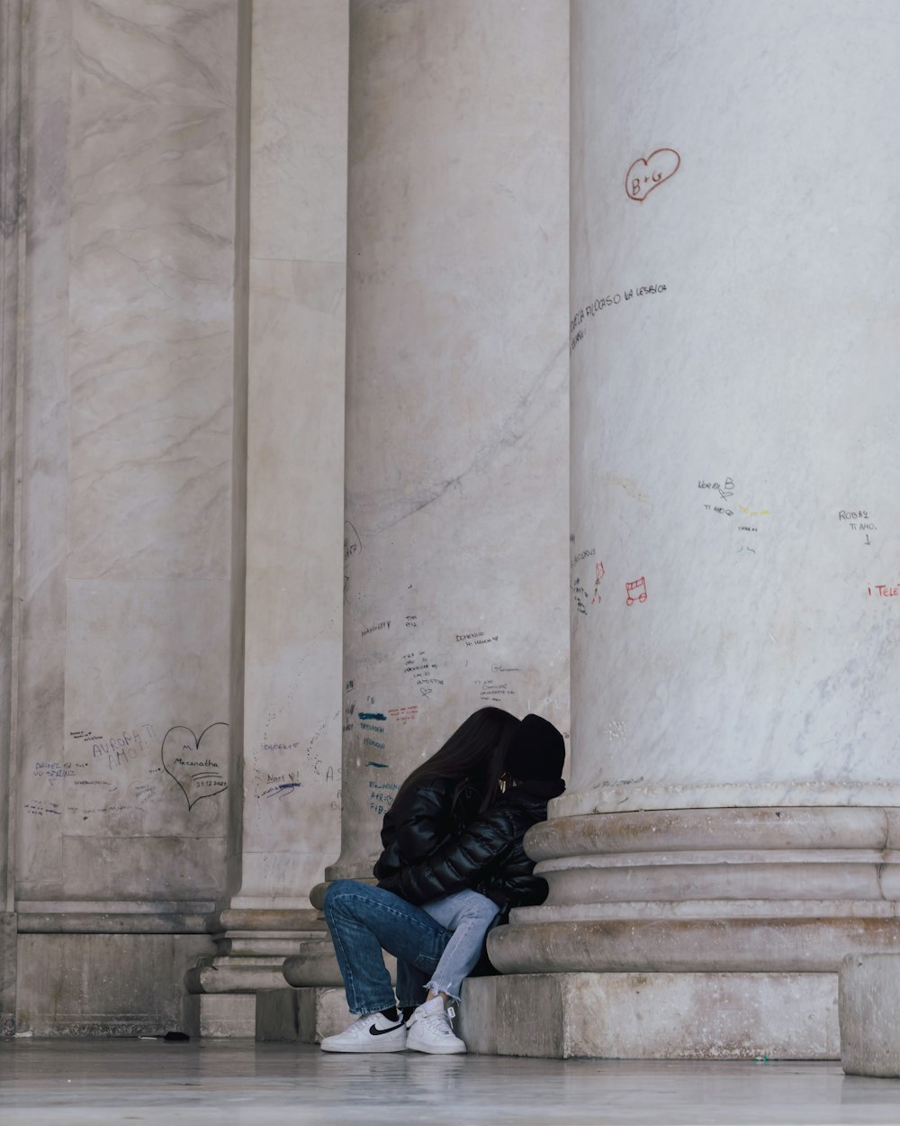 a person sitting on the ground in front of a pillar