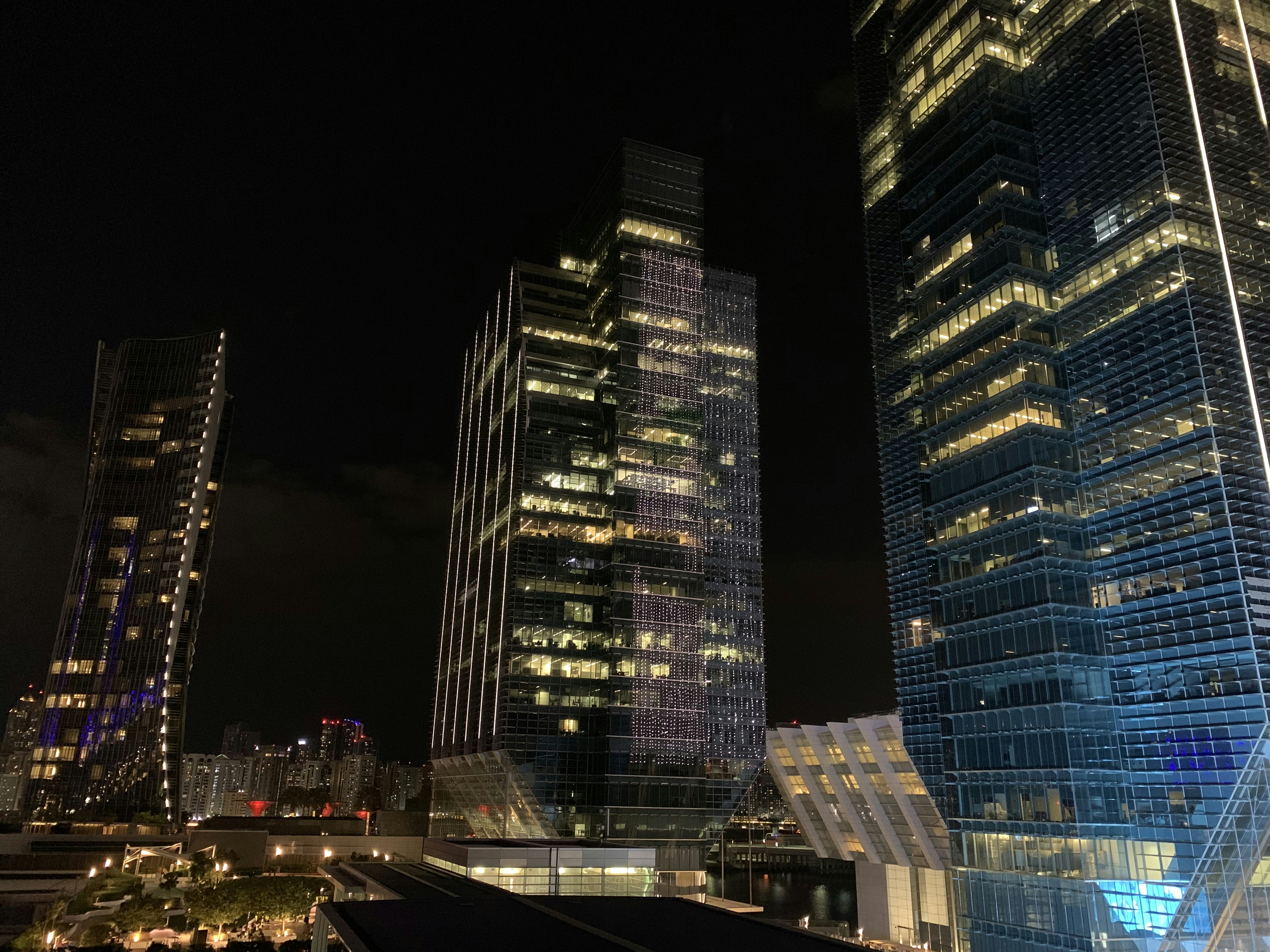 Modern architectural skyscrapers at night, dramatic upward perspective, deep shadows, city lights reflected on dark glass facades