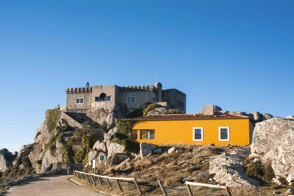 a yellow house sitting on top of a rocky hill