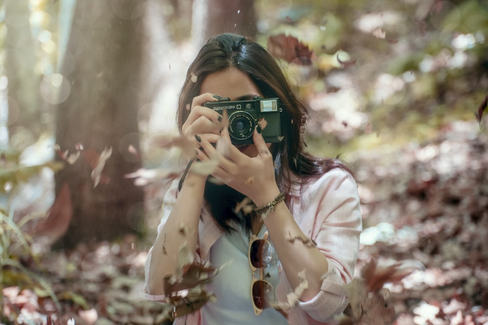 a woman taking a picture with a camera in the woods