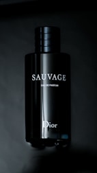 A sleek, dark bottle of fragrance with the brand name 'Sauvage' and 'Dior' visible in white letters. The bottle has a shiny, reflective surface and a simple, elegant design.