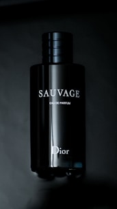 A sleek, dark bottle of fragrance with the brand name 'Sauvage' and 'Dior' visible in white letters. The bottle has a shiny, reflective surface and a simple, elegant design.