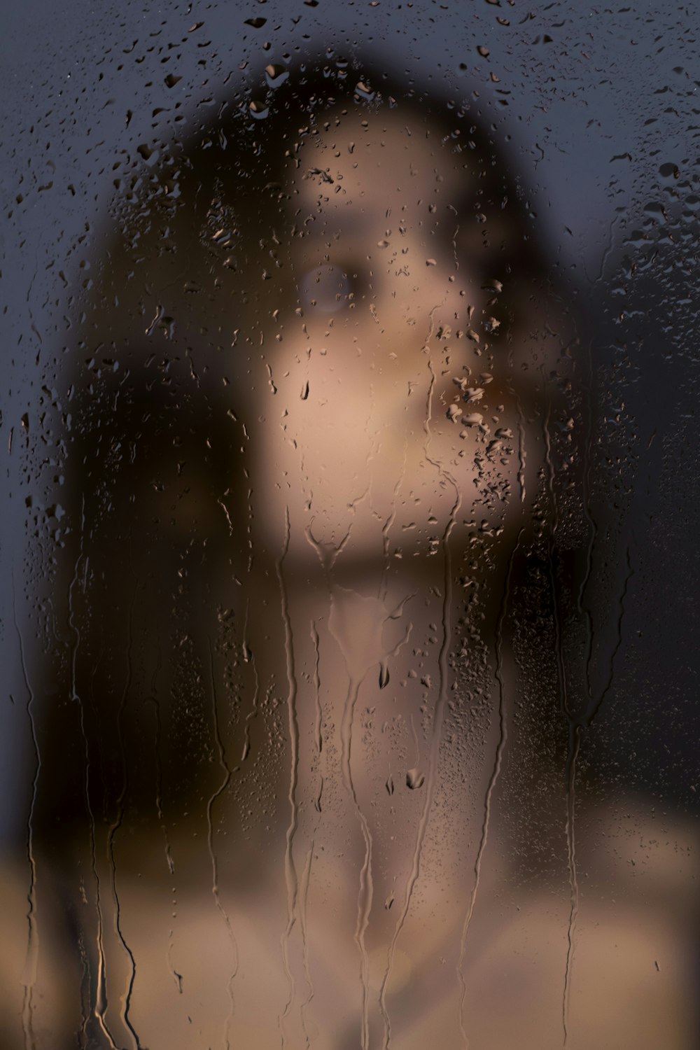 a woman standing in front of a window covered in rain