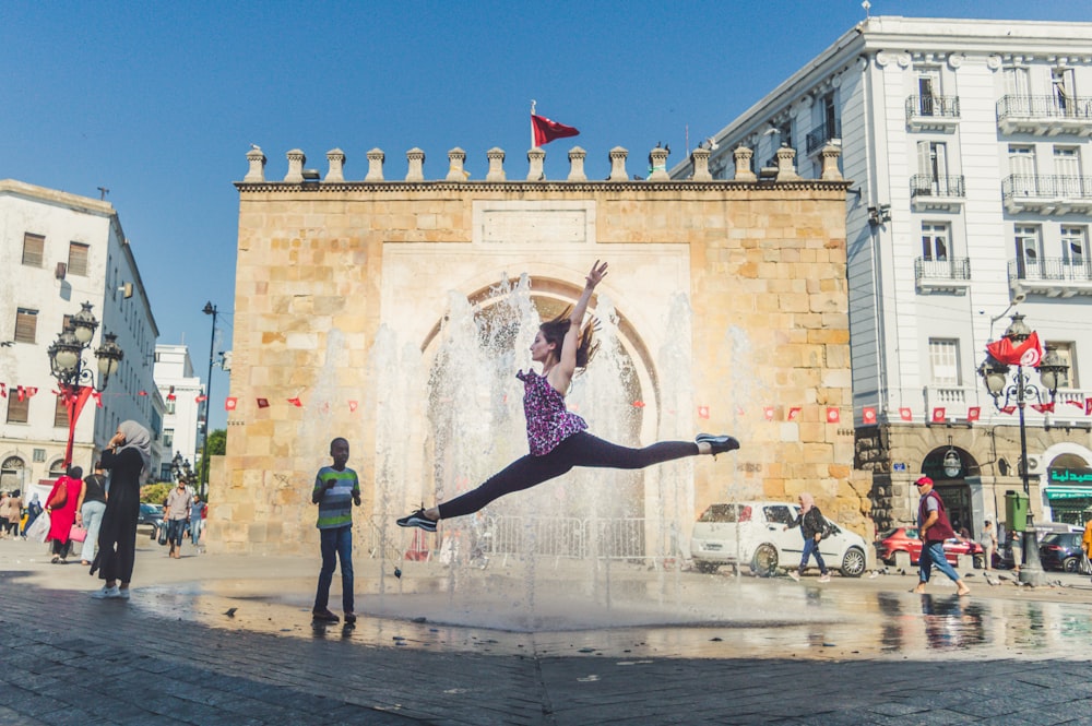 a person jumping in the air in front of a fountain