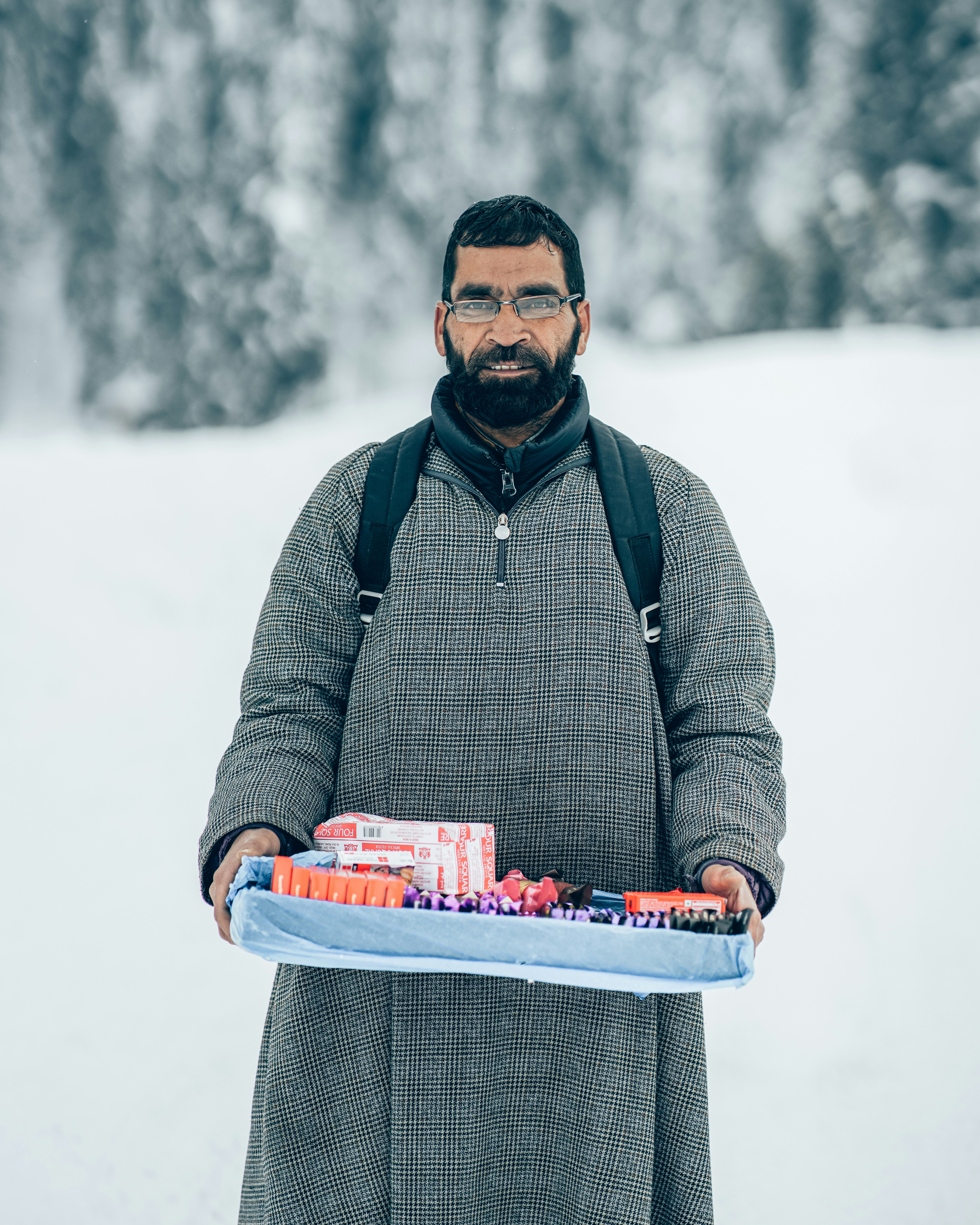 a man holding a tray of candy in the snow
