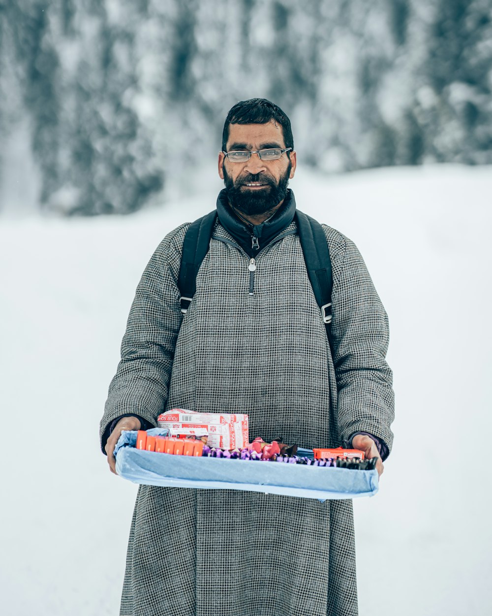 a man holding a tray of candy in the snow