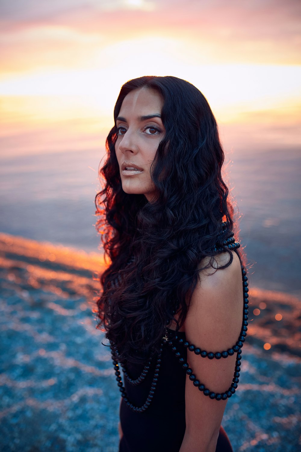 a woman with long black hair standing on a beach