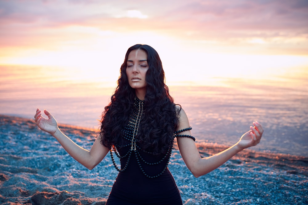 a woman in a black dress is meditating on the beach